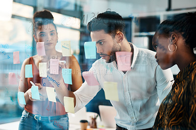 Buy stock photo Cropped shot of a diverse group of businesspeople standing and using a glass board with post-its in the office