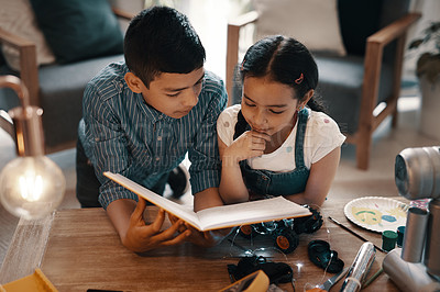 Buy stock photo Shot of two adorable young siblings reading a book about robotics together at home