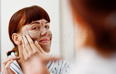 Buy stock photo Cropped shot of an attractive young woman applying a mud mask on her face while standing in front of the mirror in her bathroom at home