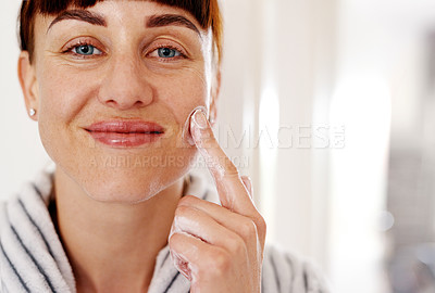Buy stock photo Cropped portrait of an attractive young woman looking cheerful while applying moisturizer on her face at home