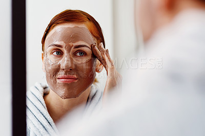 Buy stock photo Cropped shot of an attractive young woman applying a mud mask on her face while standing in front of the mirror in her bathroom at home