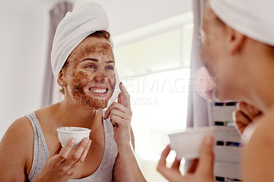 Buy stock photo Cropped shot of an attractive young woman applying a coffee mask on her face while standing in front of the mirror in her bathroom at home