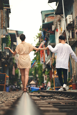 Buy stock photo Rearview shot of a young couple walking on the train tracks through the streets of Vietnam