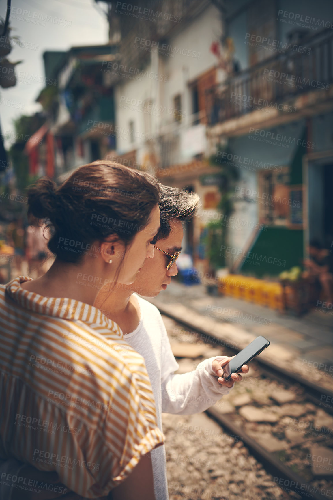Buy stock photo Shot of a young couple using a smartphone while waiting for their train to arrive in Vietnam