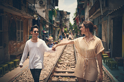 Buy stock photo Shot of a young couple walking on the train tracks through the streets of Vietnam