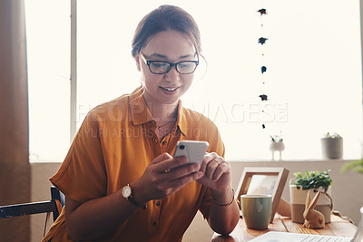 Buy stock photo Cropped shot of an attractive young businesswoman sitting alone in her home office and texting on her cellphone
