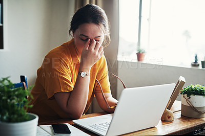 Buy stock photo Cropped shot of an attractive young businesswoman sitting alone in her home office and feeling stressed while using her laptop