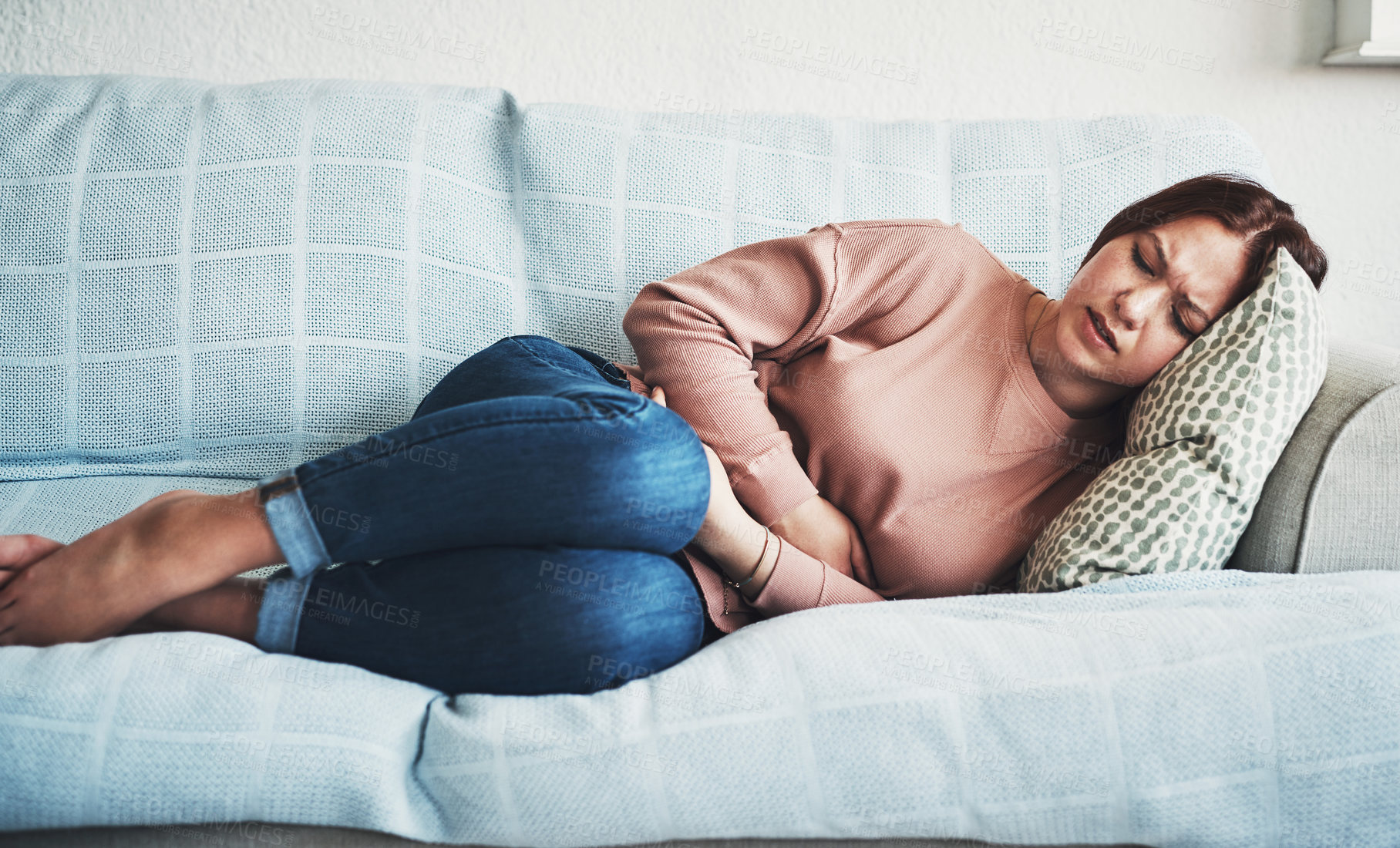 Buy stock photo Woman, stomach ache or pain on home sofa with menstrual or period cramps in lounge. Sick, abdomen or colon problem of a female person with hands on tummy for constipation, digestion or virus