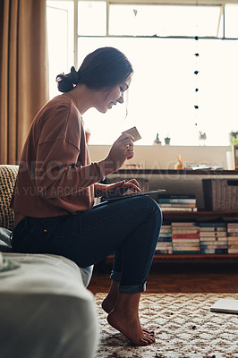 Buy stock photo Full length shot of an attractive young woman sitting on her home sofa and using a tablet for online shopping