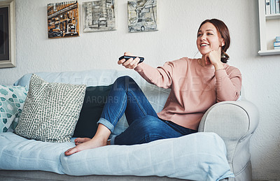 Buy stock photo Full length shot of an attractive young woman sitting on her home sofa alone and using a television remote control