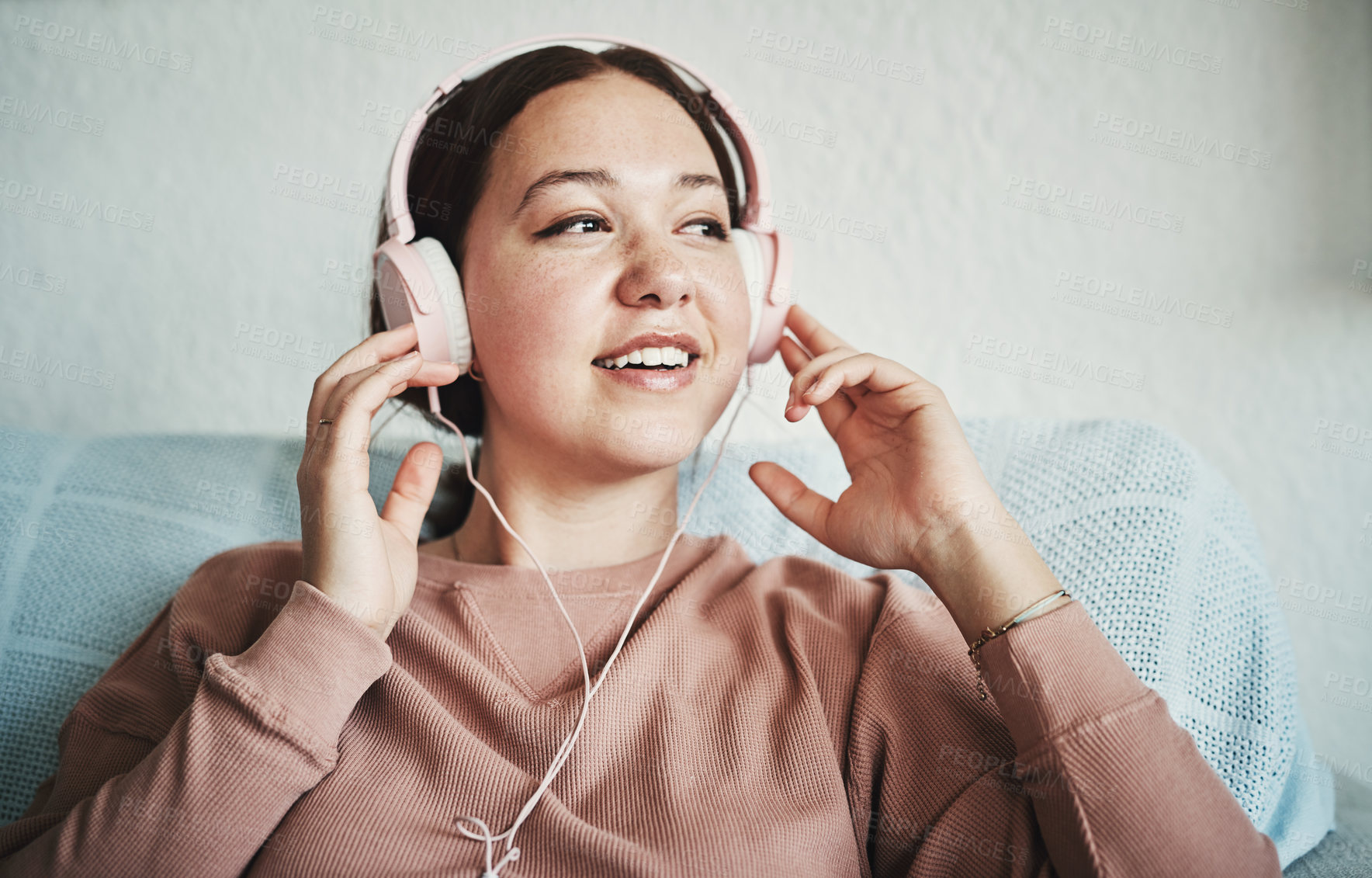 Buy stock photo Cropped shot of an attractive young woman sitting on her home sofa alone and listening to music through headphones