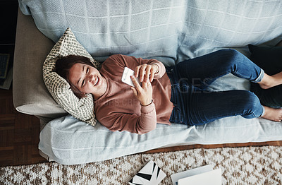 Buy stock photo High angle shot of an attractive young woman lying on her home sofa alone and texting on her cellphone
