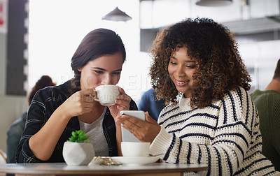 Buy stock photo Shot of two young women looking at something on a cellphone in a cafe