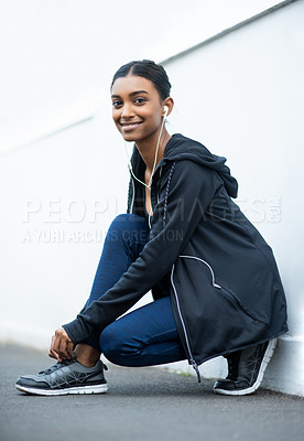 Buy stock photo Portrait of a sporty young woman tying her shoelaces while exercising outdoors