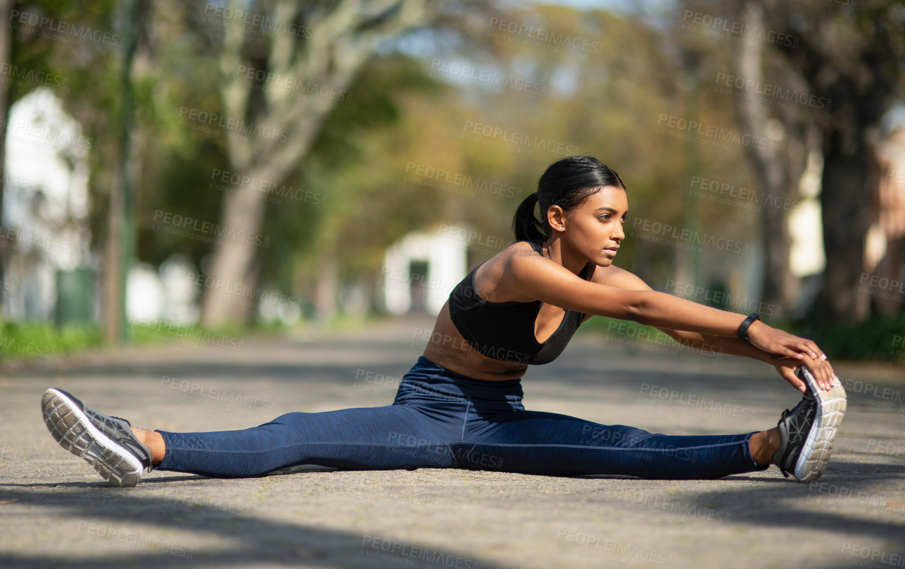 Buy stock photo Shot of a sporty young woman stretching her legs while exercising outdoors