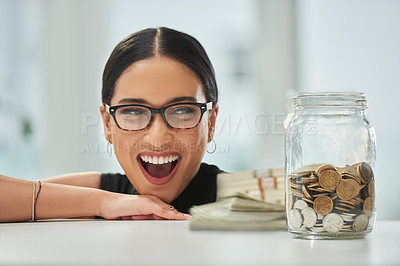 Buy stock photo Cropped shot of an attractive young businesswoman looking excitedly over at a jar of coins and wads of cash in her office