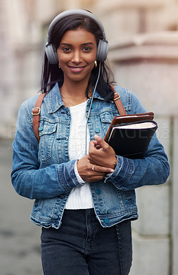 Buy stock photo Shot of a young woman walking through the city wearing headphones while carrying her books