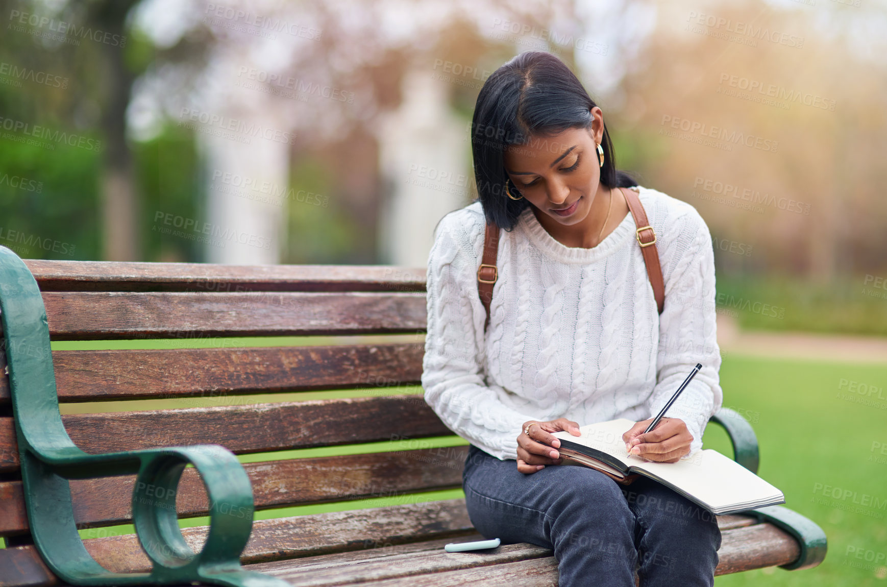 Buy stock photo Indian girl, student and writing notes at park for education, learning or studying at university on bench in garden. Notebook, serious and woman at outdoor campus for knowledge, information or course