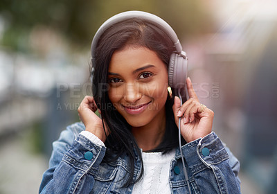 Buy stock photo Cropped shot of a young woman listening to music through her headphones while walking outdoors