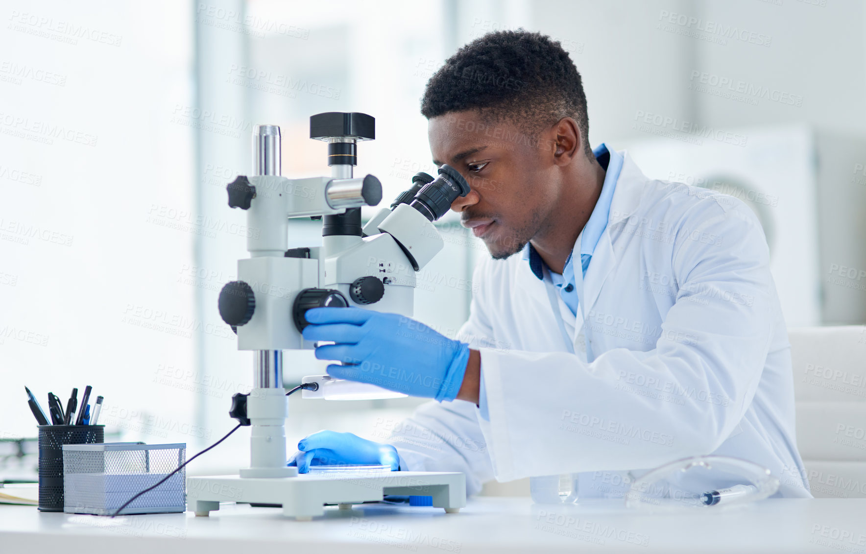 Buy stock photo Cropped shot of a focused young male scientist looking at test samples through a microscope inside of a laboratory during the day