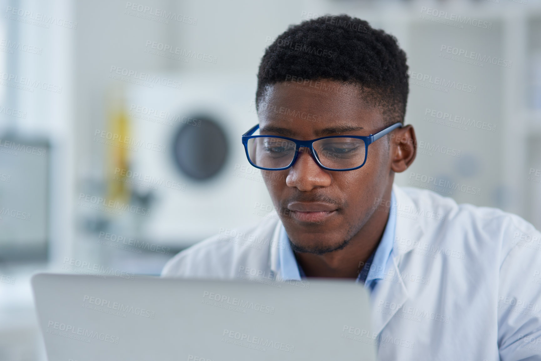 Buy stock photo Cropped shot of a focused young male scientist working on his laptop while being seated inside of a laboratory