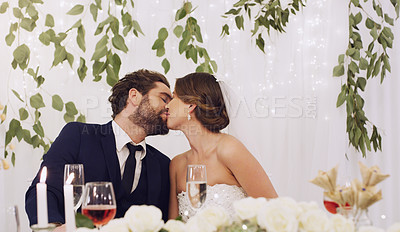 Buy stock photo Cropped shot of an affectionate young newlywed couple kissing while sitting at their wedding reception