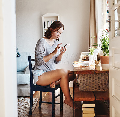 Buy stock photo Shot of a beautiful young woman using her cellphone while sitting at home