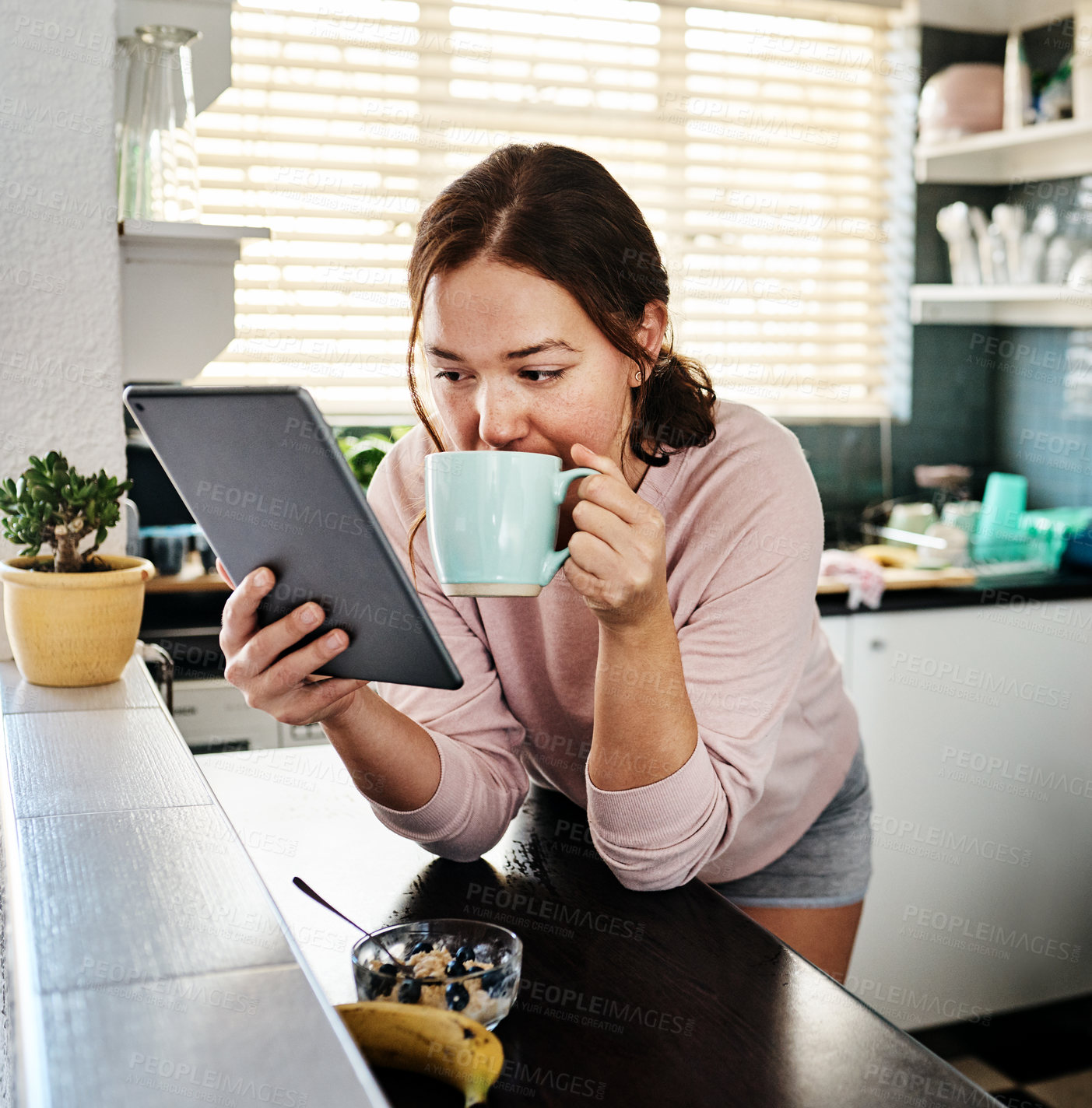 Buy stock photo Shot of a young woman drinking coffee while using a digital tablet