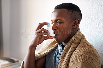 Buy stock photo Cropped shot of a handsome young man sitting alone in his bedroom and using an asthma pump