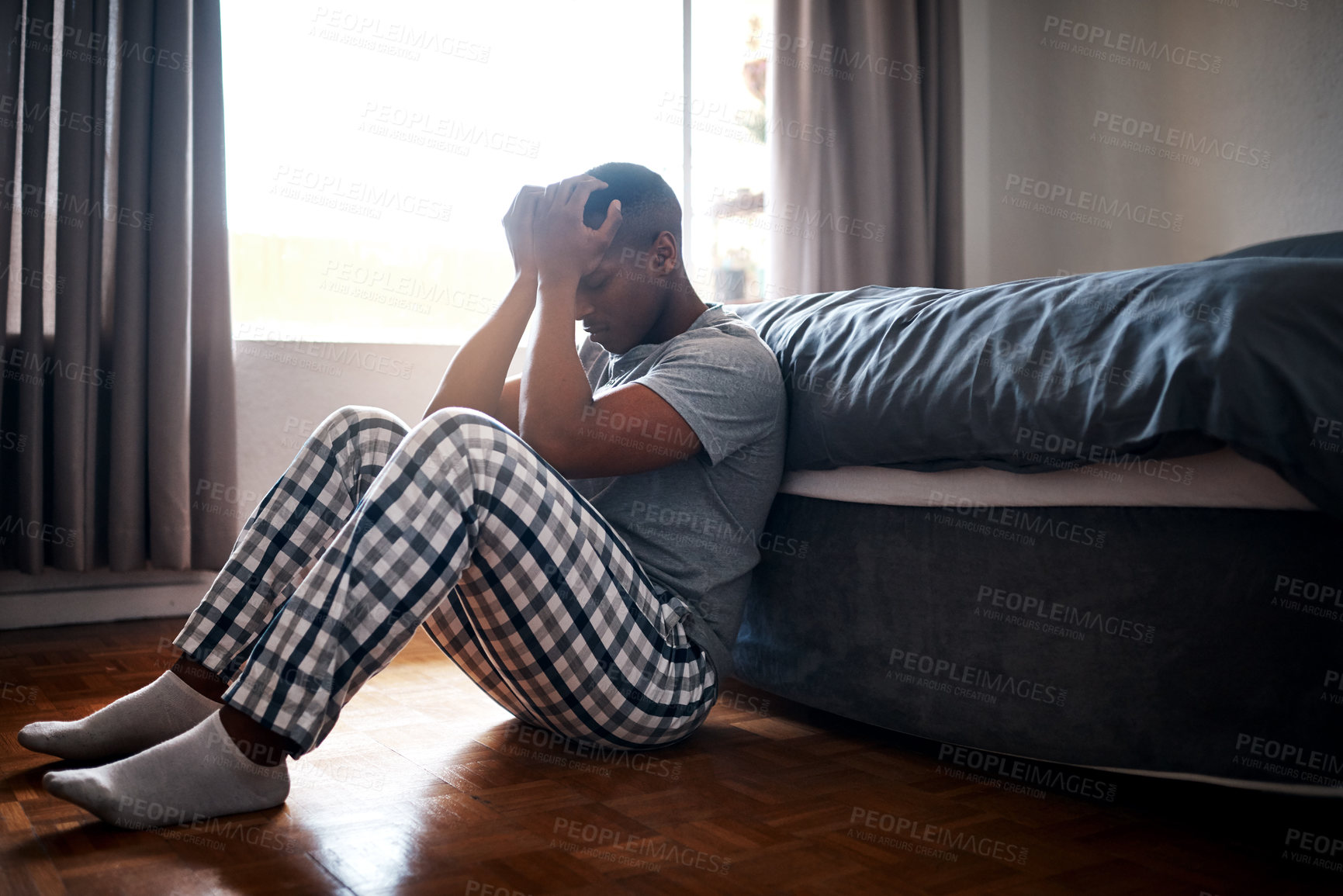 Buy stock photo Full length shot of a handsome young man sitting at the foot of his bed and feeling depressed at home