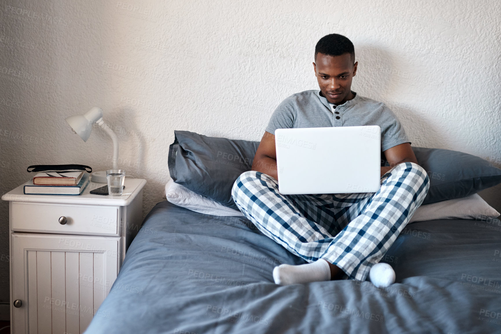 Buy stock photo Full length shot of a handsome young man sitting alone on his bed and using his laptop at home