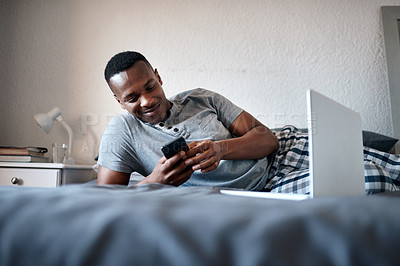 Buy stock photo Happy, laptop and black man on bed with phone for social media, online chatting and internet in bedroom. Relax, rest and person on smartphone for website, networking and message on weekend in home