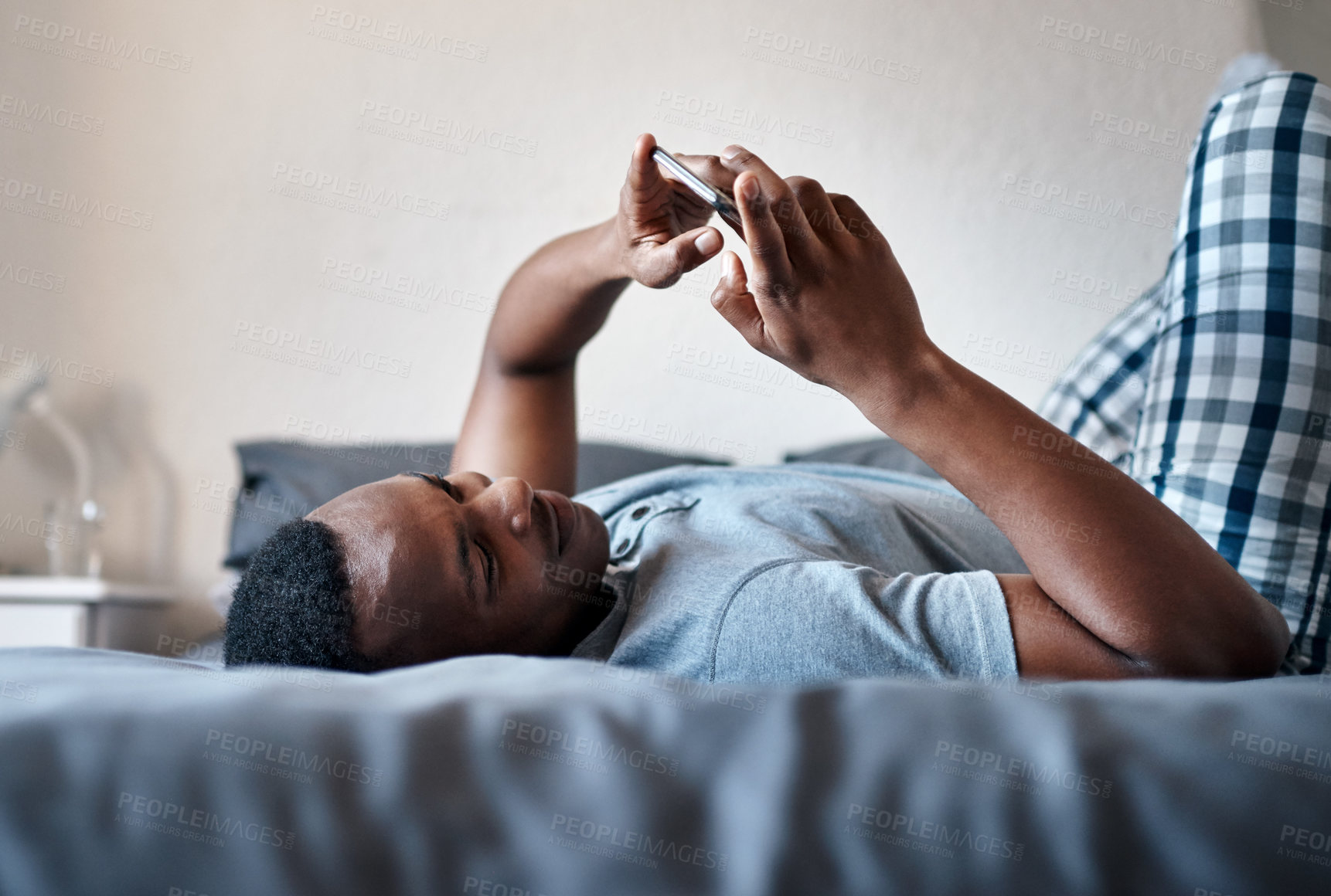 Buy stock photo Cropped shot of a handsome young man lying down on his bed and using his cellphone while at home alone