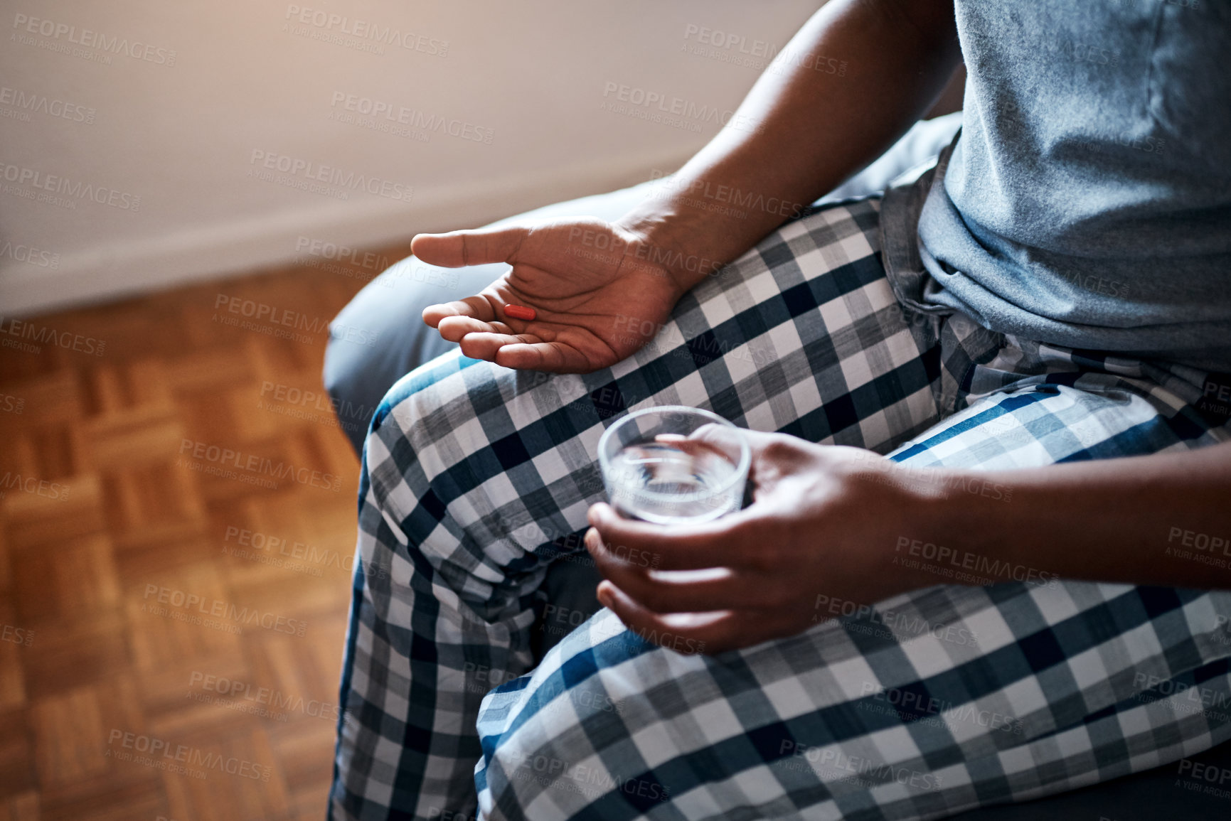 Buy stock photo Cropped shot of an unrecognizable man sitting alone on his bed and taking painkillers with water