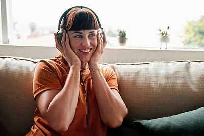 Buy stock photo Shot of an attractive young woman wearing headphones while relaxing on the sofa at home