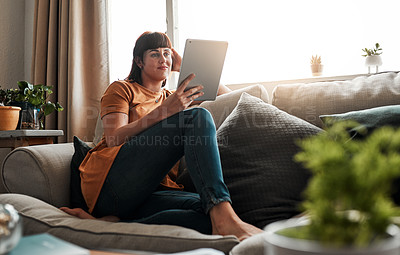 Buy stock photo Shot of an attractive young woman using a digital tablet while relaxing on the sofa at home