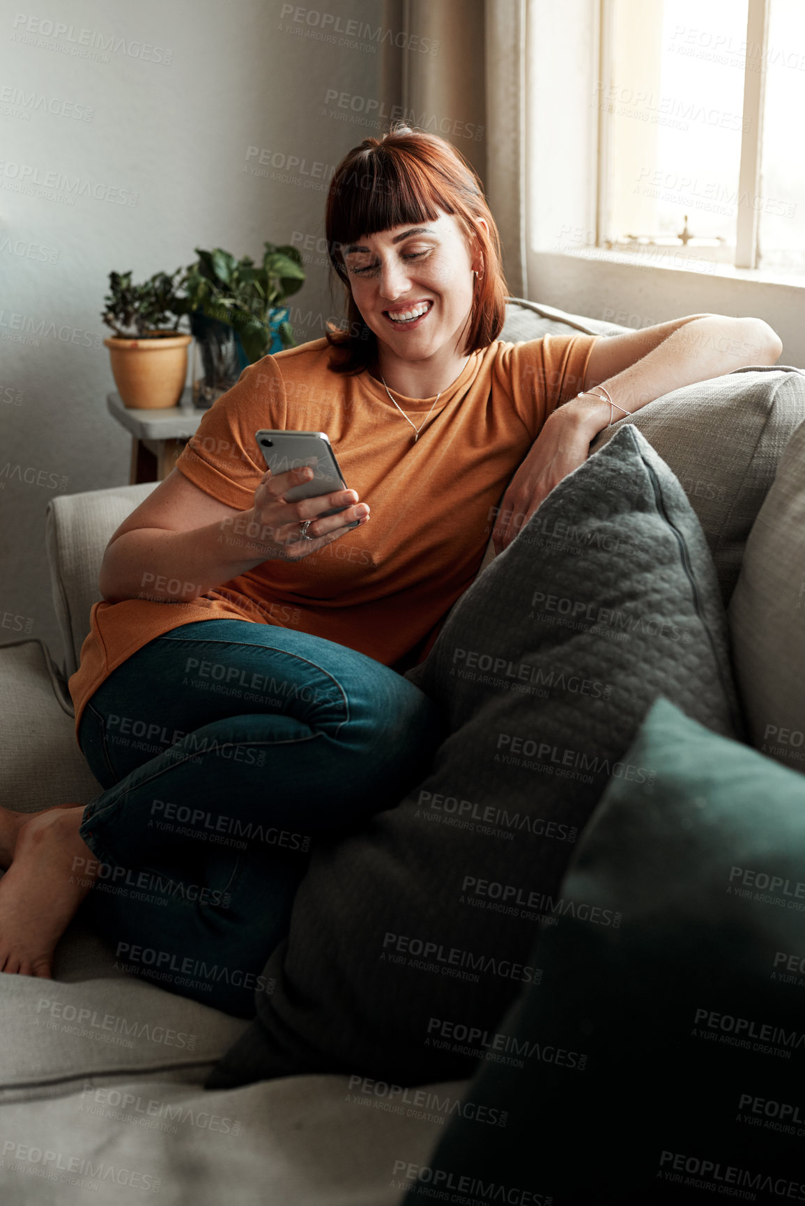 Buy stock photo Shot of an attractive young woman using her cellphone while relaxing on the sofa at home
