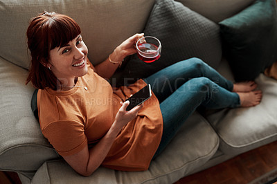 Buy stock photo Shot of a woman having a cup of tea while using her cellphone at home