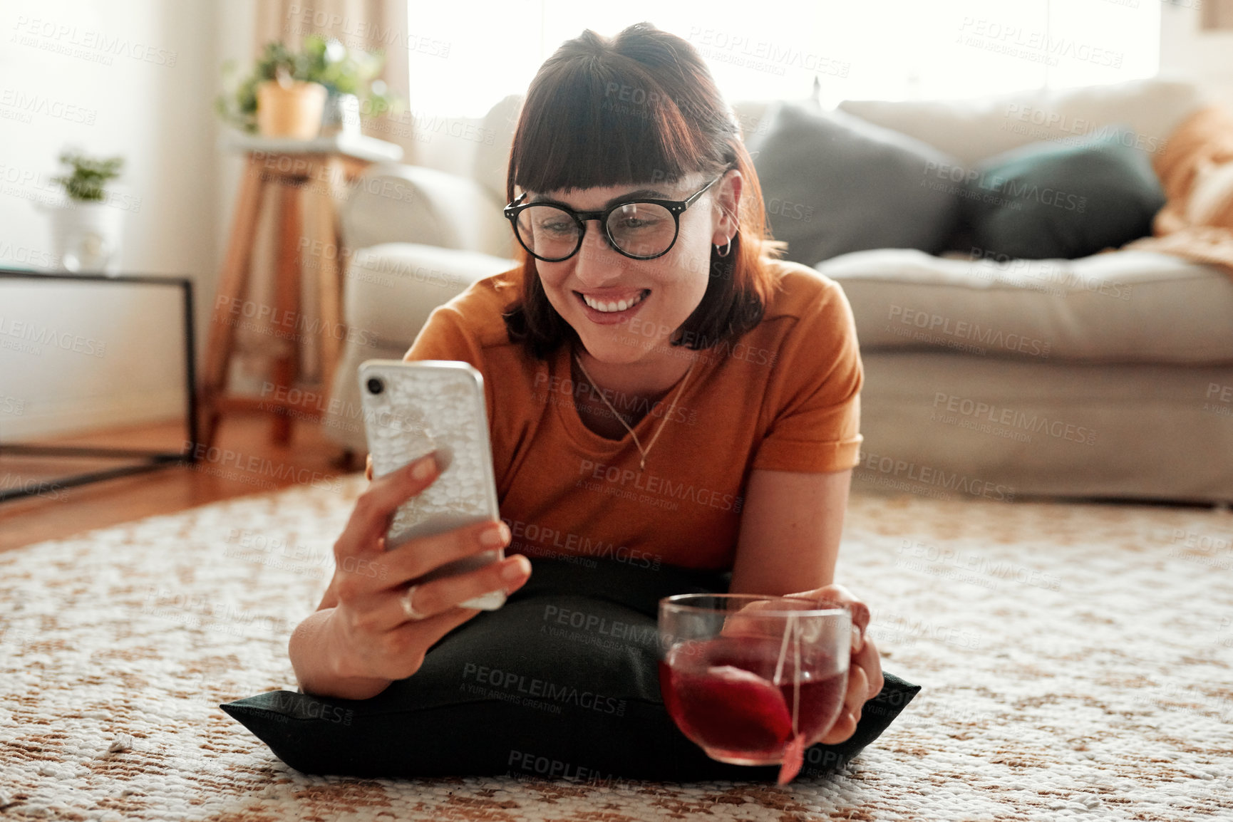 Buy stock photo Shot of a woman relaxing at home with a cup of tea and her cellphone