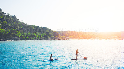 Buy stock photo Shot of a man and woman paddle boarding across the sea.