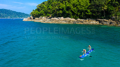 Buy stock photo Shot of a man and woman paddle boarding across the sea