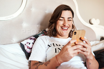 Buy stock photo Shot of a beautiful young woman using her cellphone while lying on her bed