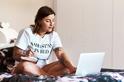 Buy stock photo Shot of an attractive young woman making notes while using her laptop