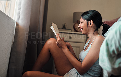 Buy stock photo Shot of a happy young woman reading a book in her bedroom