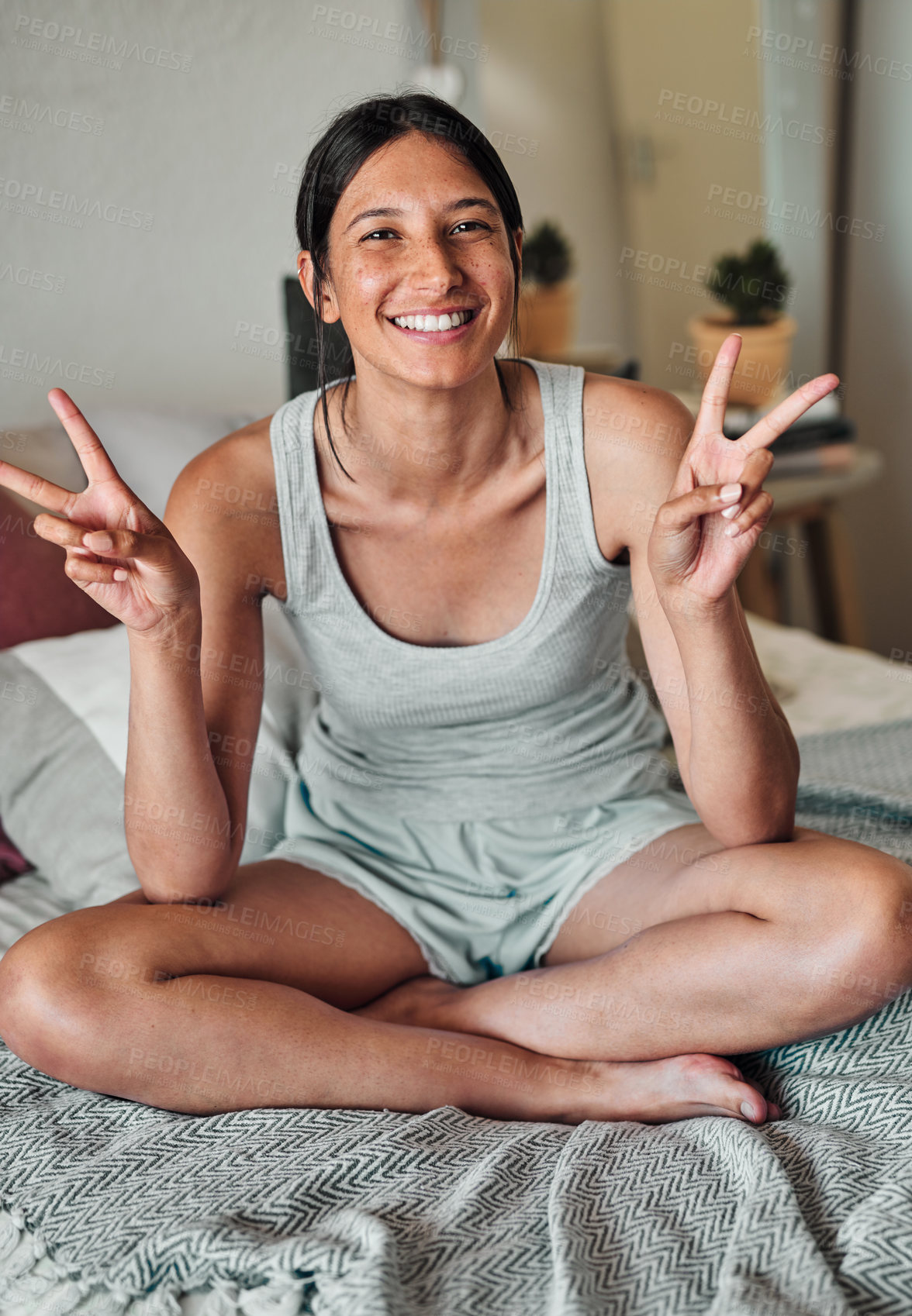 Buy stock photo Shot of a young woman relaxing on her bed and showing a peace gesture in the morning at home