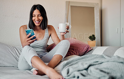 Buy stock photo Shot of a young woman using a smartphone and enjoying a cup of coffee in bed at home