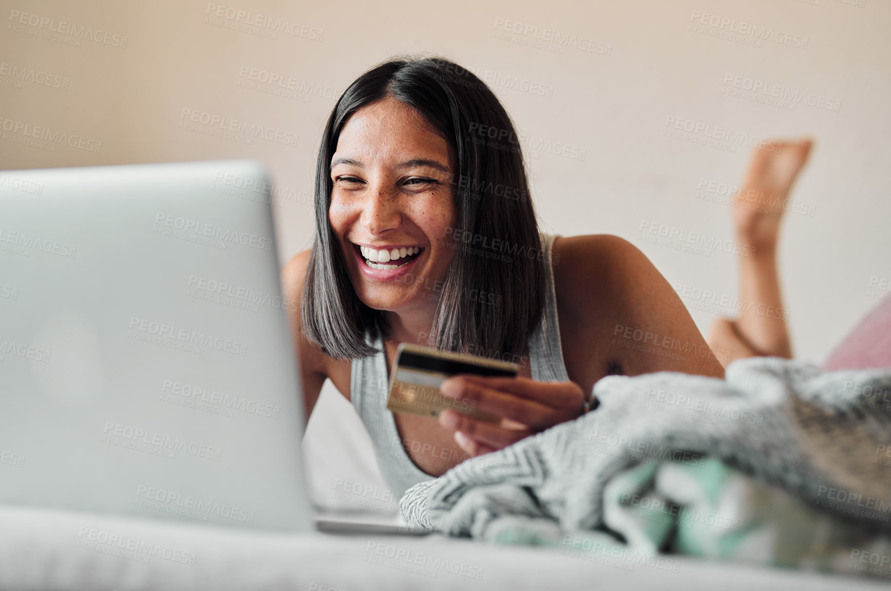 Buy stock photo Shot of a young woman using a laptop and credit card while relaxing in bed at home