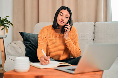 Buy stock photo Shot of a young woman using a smartphone and writing notes while working on the sofa at home