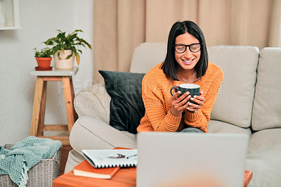 Buy stock photo Shot of a young woman having a coffee break and using a laptop while working on the sofa at home