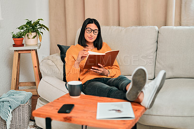Buy stock photo Shot of a young reading a book while working on the sofa at home